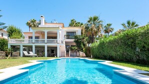 Ein zweistöckiges Haus mit Swimmingpool, umgeben von Palmen und einem gepflegten Rasen.
