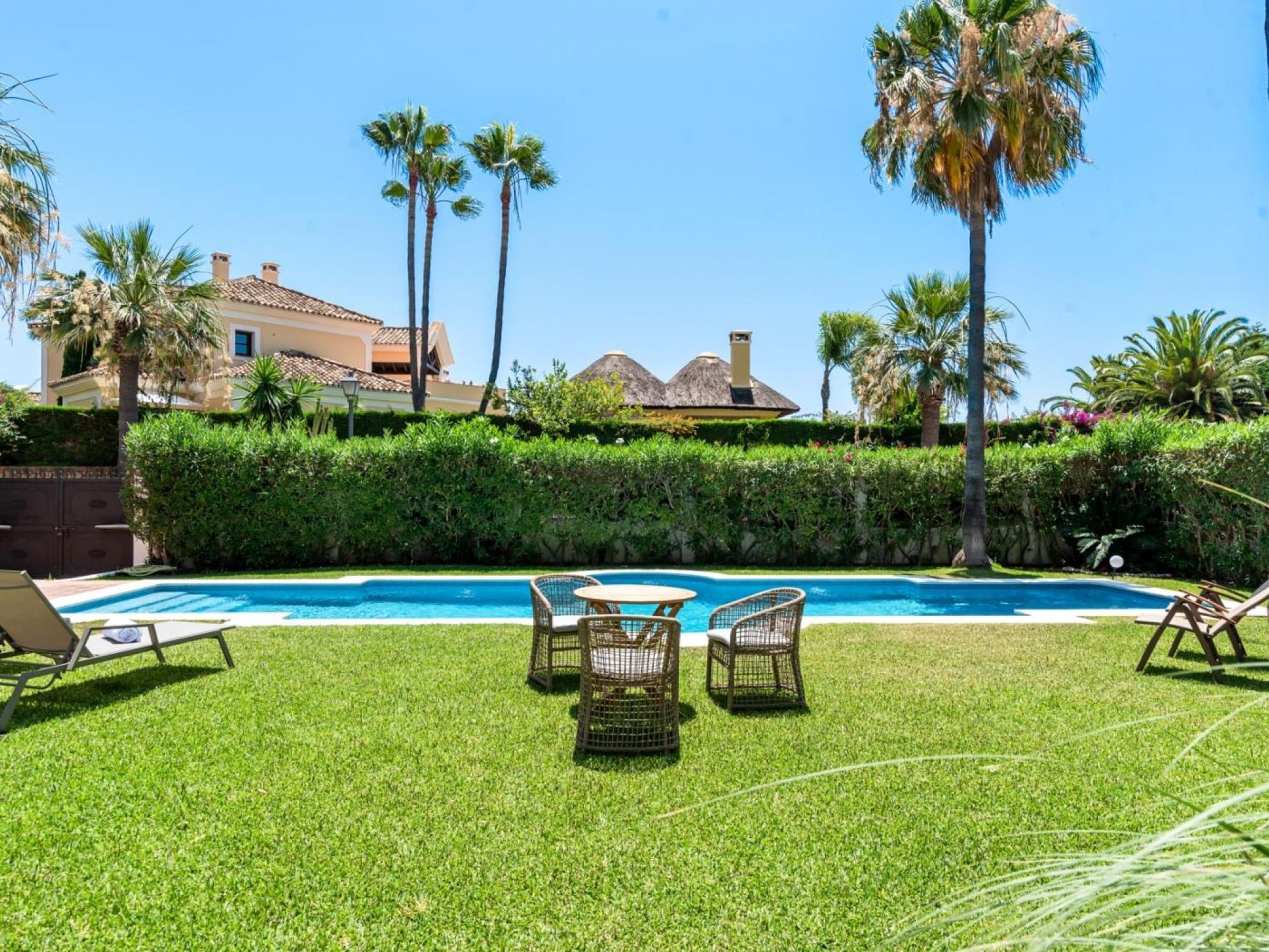 A swimming pool with lounge chairs and a table, surrounded by well-maintained grass and palm trees.