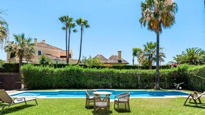 Ein Swimmingpool mit Liegestühlen und einem Tisch, umgeben von gepflegtem Rasen und Palmen.