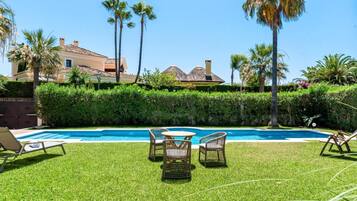 A swimming pool with lounge chairs and a table, surrounded by well-maintained grass and palm trees.