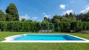 Piscina rectangular con borde blanco, rodeada de césped cuidado y un seto.