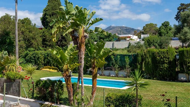 Zona residencial con piscina, abundante vegetación y una montaña al fondo.