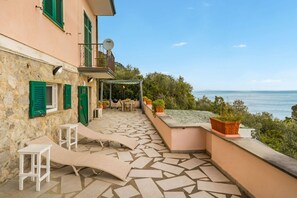 Ein Steingebäude mit Balkon und Meerblick, mit Sitzgelegenheiten im Freien und Kübelpflanzen.