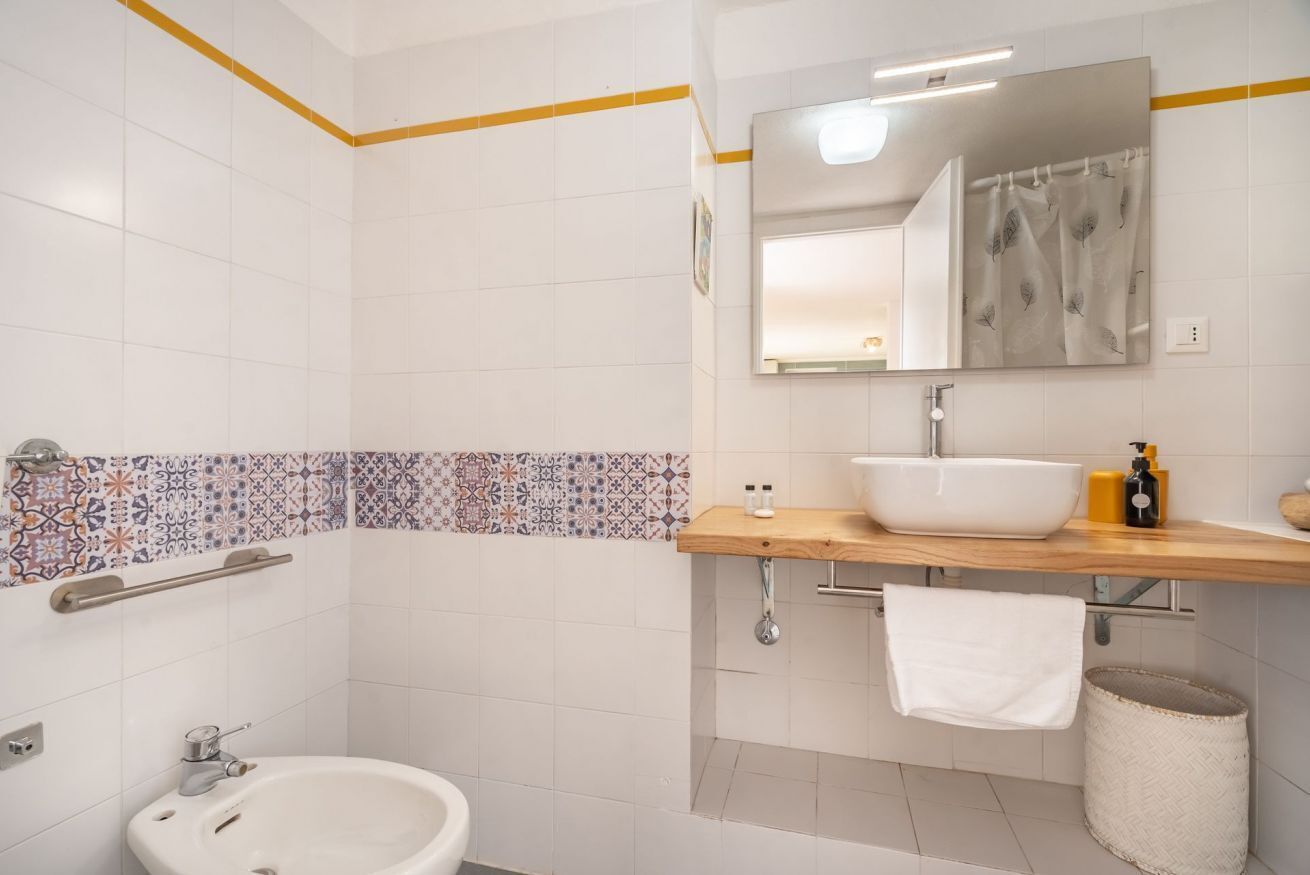 Un bagno con un lavandino bianco, uno specchio e pareti rivestite di piastrelle.