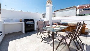 Una terraza en la azotea con una parrilla, una mesa de comedor, sillas y vistas de la ciudad.
