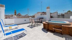 Terraza en la azotea con jacuzzi, sillas de descanso y una mesa de comedor.