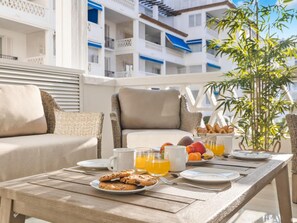 A breakfast setup with a table, chairs, and a balcony view of a building. - 3 Dormitorios en Playas del Duque Ref C2 111 (Marbella)