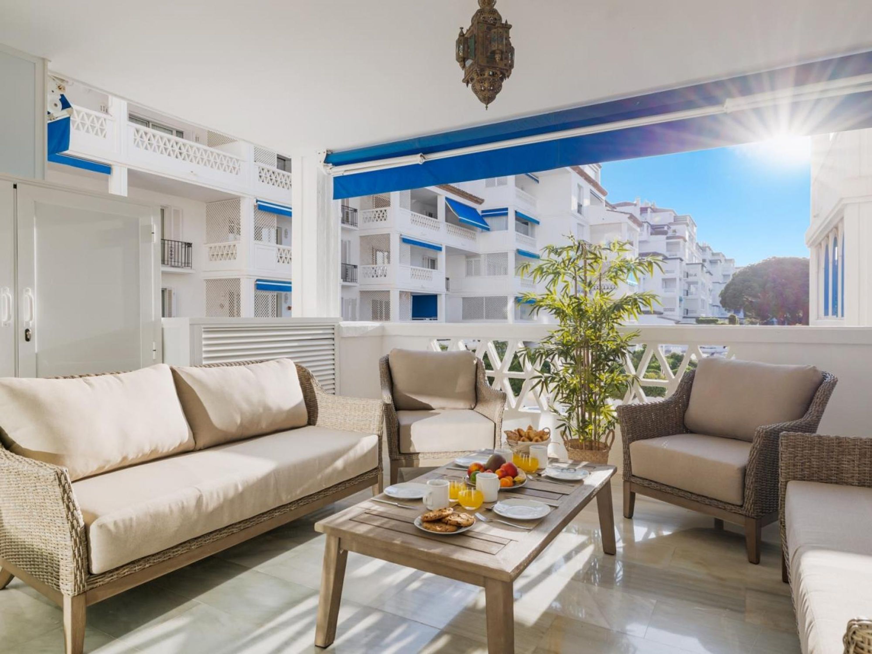 Ein Balkon mit Korbmöbeln, einem Tisch mit Frühstücksgebäck und Blick auf weiße Häuser.
