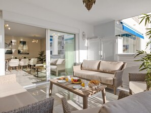 A modern living room with a sofa, chairs, a coffee table with breakfast items, and a glass door leading to a dining area. - 3 Dormitorios en Playas del Duque Ref C2 111 (Marbella)