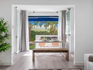 Ein Zimmer mit einem Holztisch und -stühlen, einer Bank und Blick auf einen Garten durch eine Glastür.