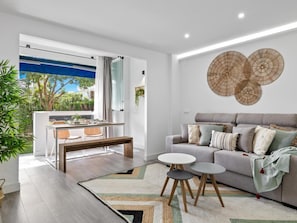 Ein modernes Wohnzimmer mit grauem Sofa, einem Couchtisch und einem Essbereich mit Tisch und Stühlen.