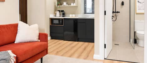 Ett kompakt bostadsutrymme med ett litet kök, en duschhörna och en röd soffa.