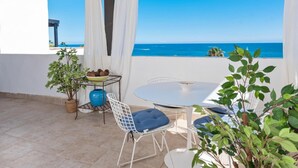 Een terras met een tafel, stoelen, een bloempot en uitzicht op zee.
