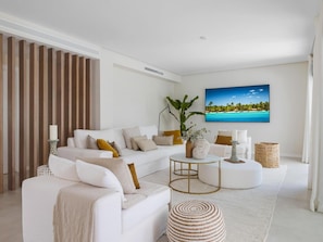 A modern living room with a white sofa, a round coffee table, and a large painting of a tropical beach. - Villa LAS Palmeras (Marbella)