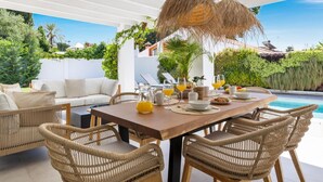 Uma área de refeições com vista para a piscina, mobiliário de vime e teto branco.