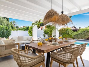 A dining area with a pool view, wicker furniture, and a white ceiling. - Villa LAS Palmeras (Marbella)
