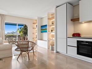 A modern kitchen with a built-in oven, a dining area with a wicker chair, and a view of the sea through large windows. - Fant Stico Apartamento con Vistas ref 751 (Marbella)