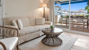 Ein modernes Wohnzimmer mit einer Couch, einem runden Couchtisch und Blick auf einen Balkon mit Gartenmöbeln.