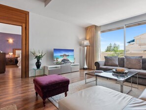A modern living room with a large window, a flat-screen TV, a sofa, a coffee table, and a small side table with a lamp. - 03 Dormitorios ref Casa Granada 146 (Marbella)