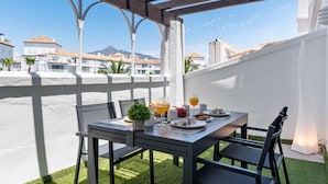 A terrace with a table set for breakfast, overlooking a coastal town with white buildings and a mountain in the distance. - 03 Dormitorios ref Casa Granada 146 (Marbella)