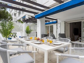 Ein weißes Esszimmer im Freien mit Korbstühlen und einem Tisch, gedeckt für ein Frühstück.