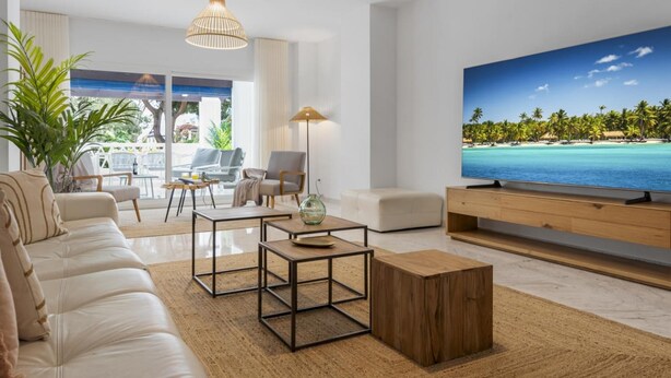 En moderne stue med et stort fladskærms-TV, en sofa, et sofabord og udsigt til en tropisk strand.