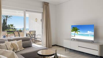 Una sala de estar moderna con un sofá, una mesa de centro, un televisor y un balcón con vistas a la playa.