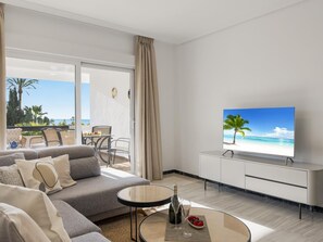 Ein modernes Wohnzimmer mit Sofa, Couchtisch, Fernseher und einem Balkon mit Blick auf den Strand.