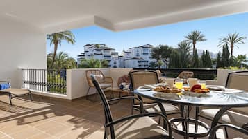 Una terraza con una mesa lista para el desayuno, con vista a una zona residencial con palmeras y edificios.