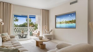 Una sala moderna con un televisor de pantalla plana grande, un sofá, una mesa de centro y un balcón con vistas a palmeras.