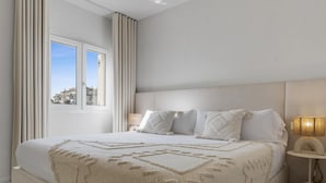 Un dormitorio moderno con una cama grande, una mesita de noche con lámpara y vistas al exterior a través de una ventana.