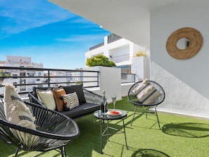 A rooftop terrace with a black sofa, two wicker chairs, a small table with a glass of wine, and a round mirror on the wall. - Confortable y c Ntrico en Terrazas de Ban s (Marbella)