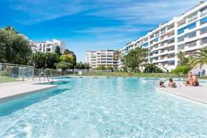 A swimming pool with clear blue water, surrounded by modern buildings and greenery. - Confortable y c Ntrico en Terrazas de Ban s (Marbella)