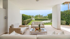 A modern outdoor seating area with a sofa, armchairs, and a coffee table, overlooking a well-manicured garden and a pool. - Amazing Ultra Modern Oasis In Atalaya (Estepona)