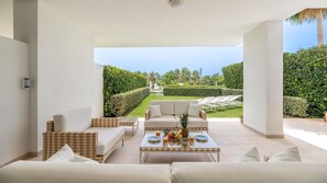 Ein moderner Außenbereich mit einer Couch, Sesseln und einem Couchtisch, mit Blick auf einen gepflegten Garten und ein Schwimmbad.