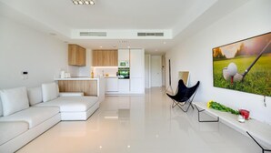 A modern living room with a white sofa, a dining area with wooden cabinets, and a kitchen with white appliances. - Amazing Ultra Modern Oasis In Atalaya (Estepona)