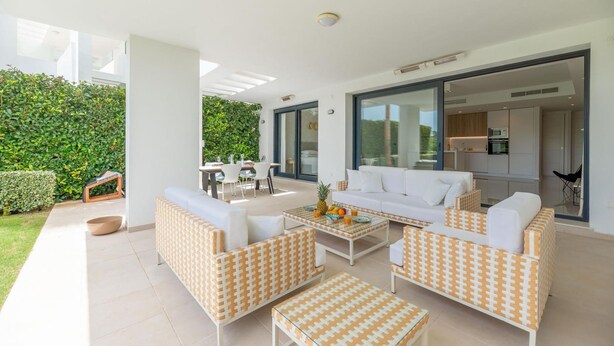 A modern outdoor living area with a sofa set, a dining table, and a kitchen visible through glass doors. - Amazing Ultra Modern Oasis In Atalaya (Estepona)