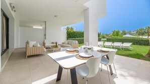 A modern outdoor patio with a dining table set for four, surrounded by white chairs and a sofa. - Amazing Ultra Modern Oasis In Atalaya (Estepona)