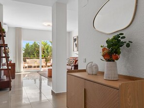 Ein modernes Wohnzimmer mit einem Holzkabinett, einer weißen Vase mit Blumen und einem großen Spiegel an der Wand.