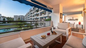 A balcony with a view of a pool and buildings, a table with food, and a chair. - Urban Exclusivity At Puerto Ban s (Marbella)