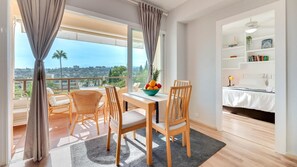 A modern room with a balcony, a dining table with chairs, a bed, and a bookshelf. - Charming Golfers Place Puerto Banus (Marbella)