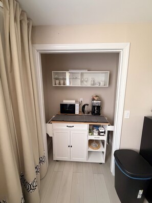 Una kitchenette compacta con microondas, cafetera y armarios de almacenamiento.
