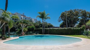 Ein Swimmingpool mit umgebender Umzäunung, Palmen und einem Gebäude im Hintergrund.