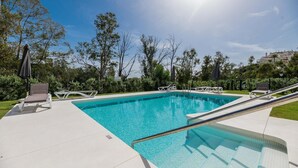 A swimming pool with lounge chairs and a sunshade, surrounded by greenery and a clear sky. - Endless Luxury At Marbella Lake Paradise (Marbella)