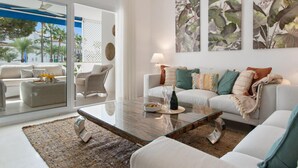 Un salon moderne avec une table basse en verre, des canapés blancs et des œuvres d’art aux motifs tropicaux.