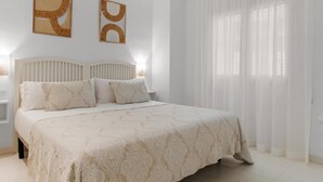Une chambre à coucher avec un grand lit, une table de chevet et deux œuvres d’art abstraites accrochées au mur.