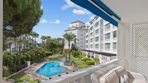 Un balcon donnant sur une piscine, une végétation luxuriante et, au loin, un immeuble à plusieurs étages.