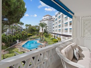 Ein Balkon mit Blick auf ein Schwimmbecken, üppiges Grün und ein mehrstöckiges Gebäude im Hintergrund.