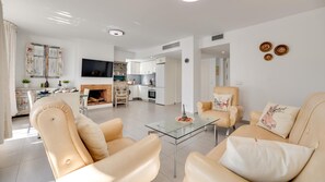 Ein modernes Wohnzimmer mit einem Glastisch, beigefarbenen Ledersofas und einem Flachbildfernseher.