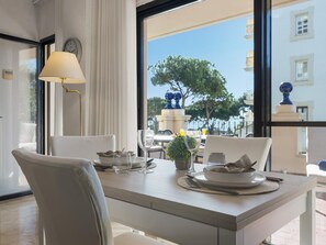 Ein Essbereich mit Tisch für zwei Personen, einer Lampe und Blick auf das Meer und die Gebäude.